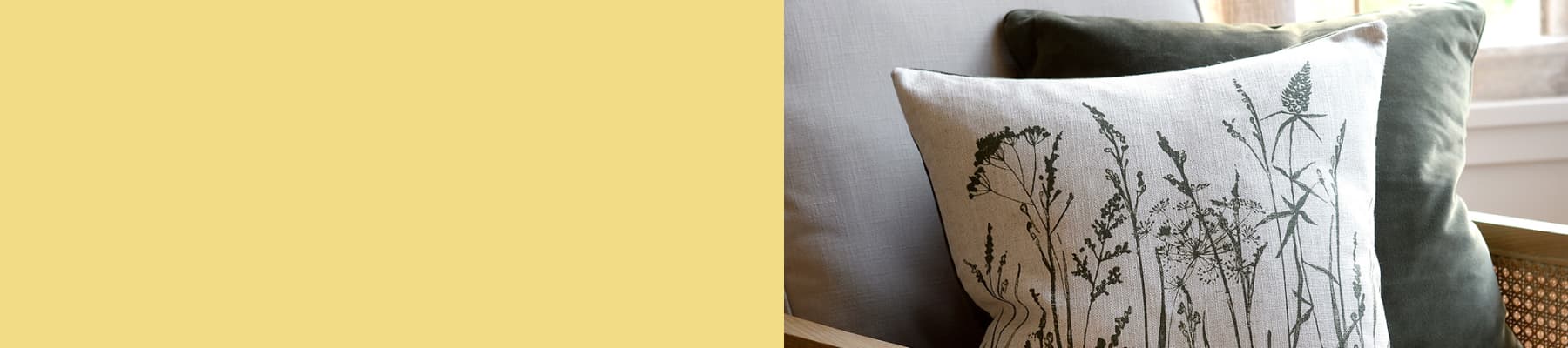 A decorative pillow with botanical designs sits on a chair with a solid green cushion.