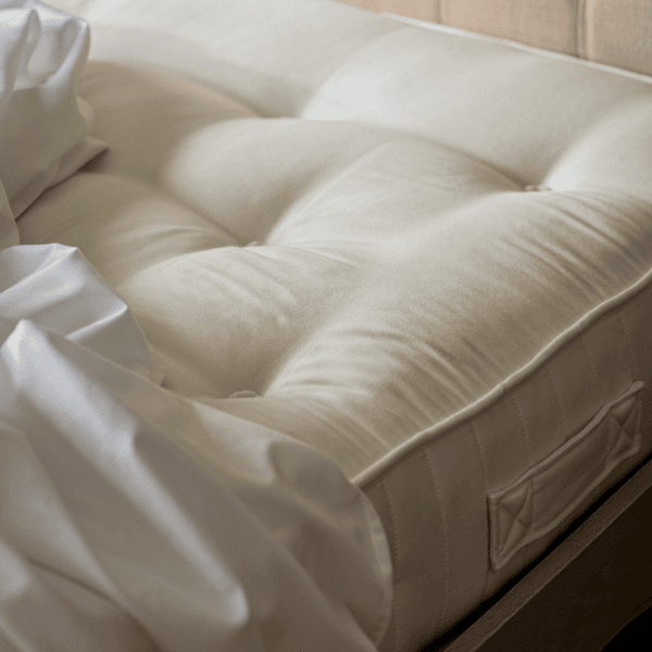 Unmade bed with a white, tufted mattress and crumpled white sheets, creating a cozy and inviting appearance.