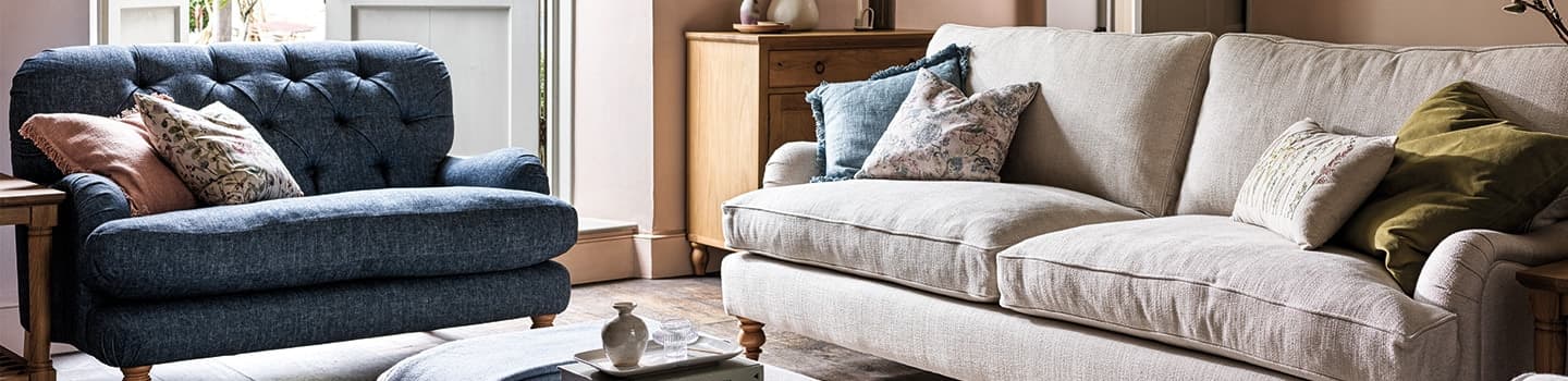 Cozy living room with a blue armchair, beige sofa, assorted cushions, and a wooden side table by a window.